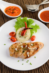 Grilled chicken on a white plate with tomatoes, salad, onion, chili and sauce.