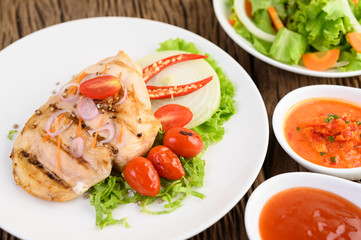Fototapeta na wymiar Grilled chicken on a white plate with tomatoes, salad, onion, chili and sauce.