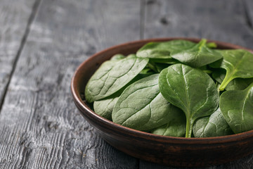 Bright fresh spinach leaves in a clay bowl on a wooden table. Food for fitness.
