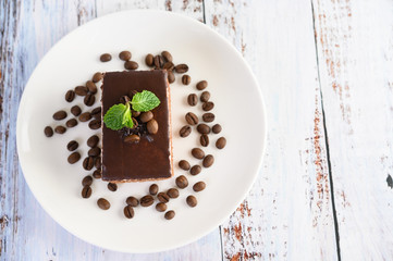 Chocolate cake on a white plate with coffee beans on a wooden table