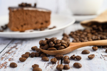 Coffee beans on wooden spoon on a white wood table.
