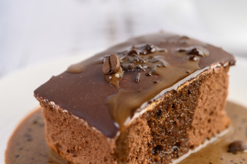 Chocolate cake topped with coffee on a white plate with coffee beans on a wooden table.
