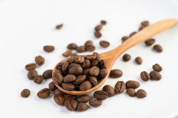 Coffee beans on wooden spoon on a white wood table.