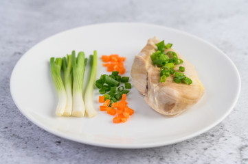 Steamed chicken breast on a white plate with spring onions and chopped carrots