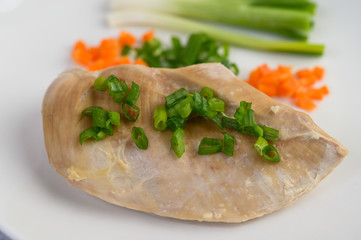 Steamed chicken breast on a white plate with spring onions and chopped carrots
