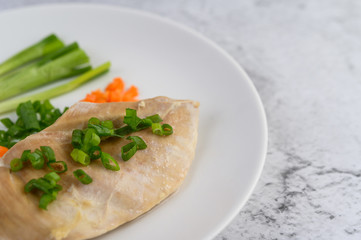 Fototapeta na wymiar Steamed chicken breast on a white plate with spring onions and chopped carrots