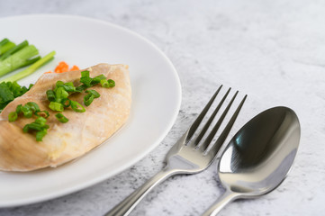 Steamed chicken breast on a white plate with spring onions and chopped carrots