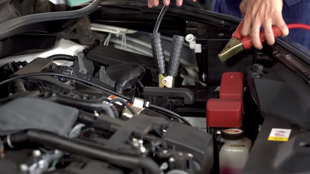 mechanic hand charging battery car with electricity through jumper cables