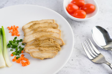 Steamed chicken breast on a white plate with spring onions and chopped carrots