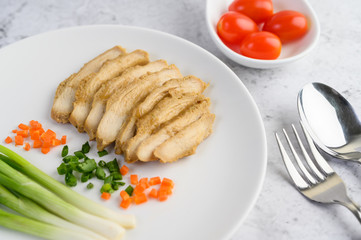 Steamed chicken breast on a white plate with spring onions and chopped carrots