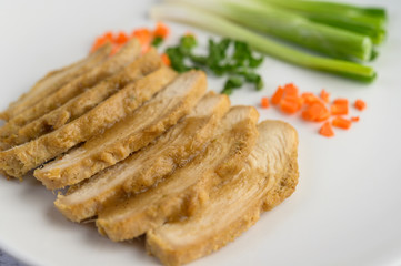 Steamed chicken breast on a white plate with spring onions and chopped carrots