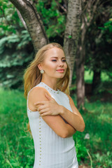 Fototapeta premium Portrait of a charming blond woman wearing beautiful white dress standing next to rowan tree.