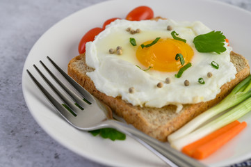 A fried egg laying on a toast, topped with pepper seeds with carrots and spring onions.