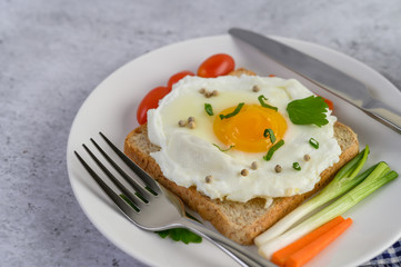 A fried egg laying on a toast, topped with pepper seeds with carrots and spring onions.