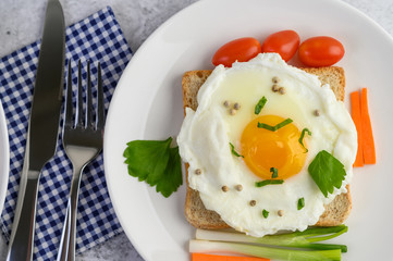 A fried egg laying on a toast, topped with pepper seeds with carrots and spring onions.