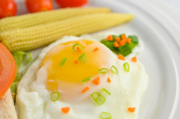 Naklejka na ściany i meble A fried egg laying on a toast, topped with pepper seeds with carrots, baby corn and spring onions.