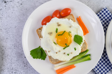 A fried egg laying on a toast, topped with pepper seeds with carrots, baby corn and spring onions.