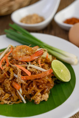 Padthai shrimp in a white dish with lime and eggs on wooden table.