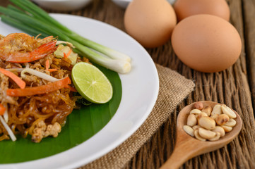 Padthai shrimp in a white dish with lime and eggs on wooden table.