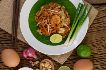 Padthai shrimp in a white dish with lime and eggs on wooden table.