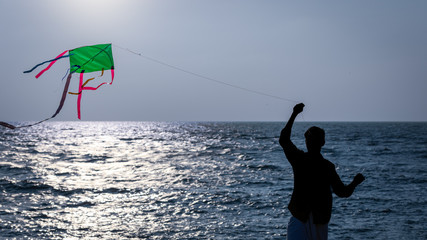 A man silhoetted against the shore waters tries to fly a home made kite