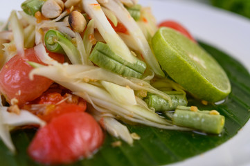 Papaya Salad (Som tum Thai) on a white plate on a wooden table.