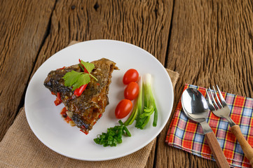 Deep-fried fish heads topped with chilies on a white plate with tomatoes and spring onions.