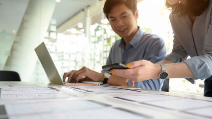 Cropped shot of UI developer working on laptop and document while consulting with co worker