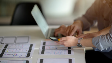 Side view of UI developer working on  laptop and document while consulting with co worker