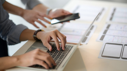 Close up view of UI developer typing on laptop and document  while discussing with co worker