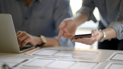 Close up view of UI developer team briefing on their project with smartphone and laptop