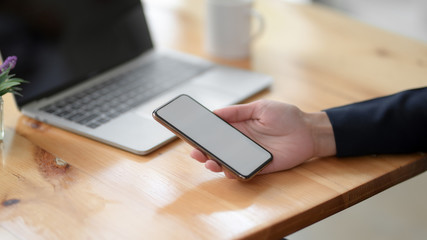 Close up view of a woman holding blank screen smartphone on wooden desk