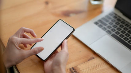 Close up view of a woman touching on blank screen smartphone on wooden desk