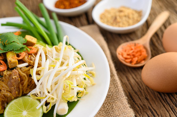 Pad Thai in a white plate with lemon, eggs and seasoning on a wooden table.