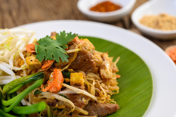 Pad Thai in a white plate with lemon, eggs and seasoning on a wooden table.