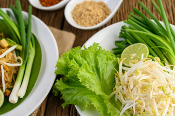 Bean sprouts, salads, lime and spring onions in white plate on wooden table