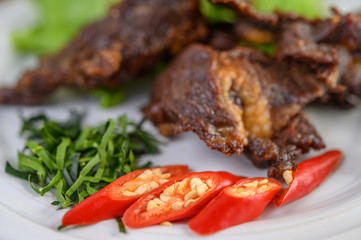Beef fried Thai food on a white plate with spring onion, kaffir lime leaves, chilies, salad and chili paste in a cup.