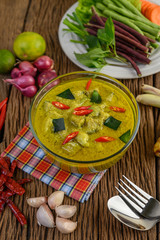 Green curry in a bowl with fork and spoon on wooden table.