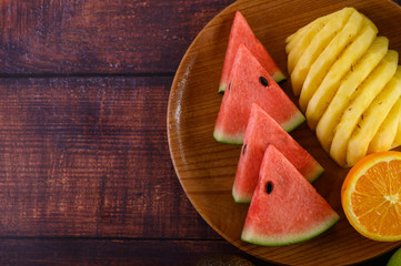 Watermelon, orange and pineapple cut into pieces on a wooden plate