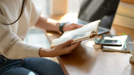 Obraz premium Cropped shot of college girl reading book while working on her assignment