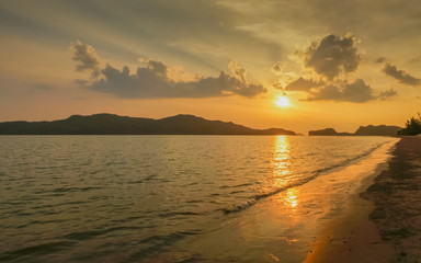 view panorama seaside evening on long beach of limestone mountain in the sea with yellow sun light and cloudy sky background, sunset at Pak Bara Beach, La-ngu District, Satun, southern Thailand.