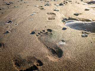 Closeup photo of footprints on the wet volcanic sand at ocean shore