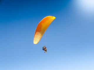 Beautiful image of professional paragliding instructor with touris tflying on the parachute against clear blue sky