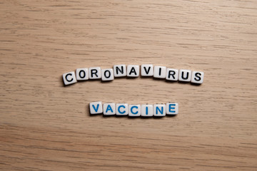 the word CORONAVIRUS VACCINE in white cubes on a light wooden background. Corona Virus design template