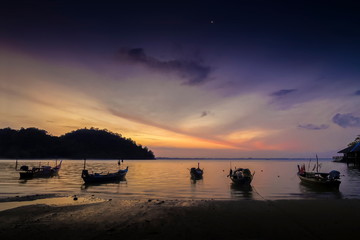 view seaside morning of fishing boats floating in the sea with orange sun light and cloudy sky background, sunrise at Mu Ko Phetra National Park, pak nam, la-ngu district, Satun, Thailand.