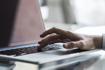 Man typing on laptop keyboard in sunny office, business and technology concept. Close up