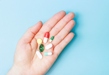 Pills and capsules in a female hand on blue background top view.