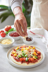 Baker's hand placing ingredients on pizza