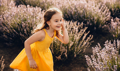 Lovely caucasian girl wearing a yellow dress is playing joyfully with her hair in a lavender field