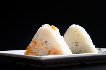Onigiri, a Japanese food that looks like a triangle or ball oval Wrapped in seaweed (Nori), is a healthy food placed on a white plate with a black background